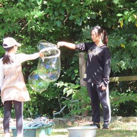 大きなしゃぼん玉を作る子どもとボランティア