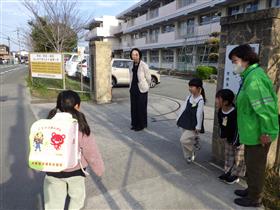 正門前で登校した児童とやりとりをする校長先生とボランティアの児童