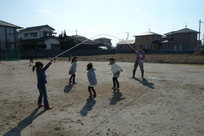 空き地で子どもたちが大繩をしている写真