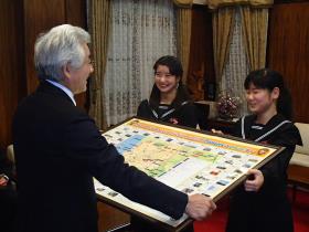 英語版ポスター「大牟田の宝もの」を市長に手渡す米生中生徒2人